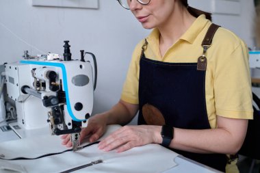 Tecrübeli bronzlaştırıcı, deri giysi parçalarını yan yana dikerken masa başında elektrikli ekipmanlarla oturuyor.