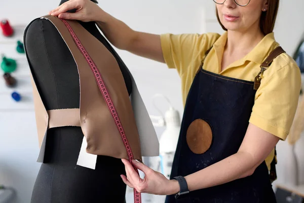 Close-up of creative leather worker or tailor measuring front part of new waistcoat on mannequin while standing in front of camera