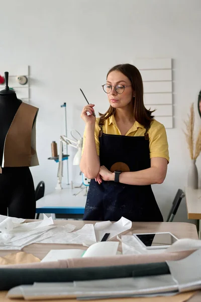Pensive Female Seamstress Apron Standing Front Workplace Sewing Paper Patterns — Stock Photo, Image