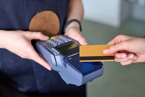 Hands of shop assistant holding card reader during contactless payment of customer for purchase of leatherwear in small craft studio or atelier