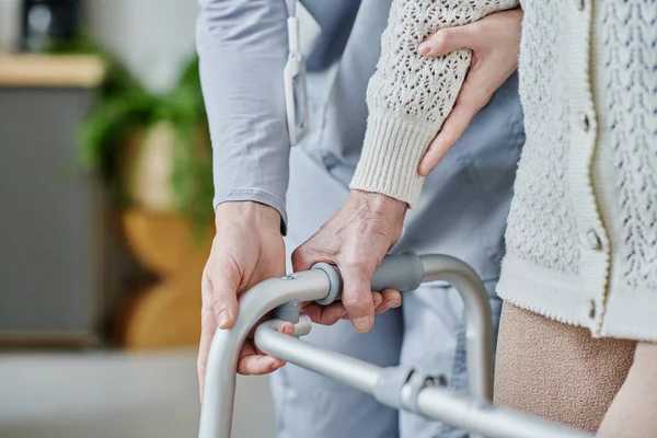 介護者のクローズアップは 高齢女性がウォーカーを使って歩くのを助ける — ストック写真