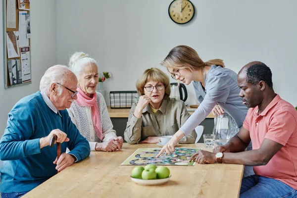 Giovane Caregiver Raccontando Regola Del Gioco Agli Anziani Mentre Siedono — Foto Stock