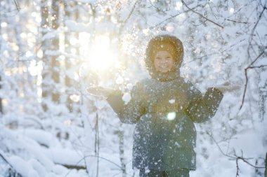 Küçük kızın portresi kış ormanlarında yürürken karla eğleniyor.