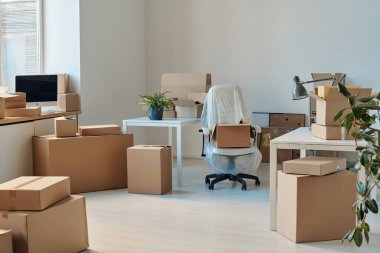 Mobilyaları ve paketlenmiş karton kutuları olan büyük ışıklı ofisin yatay görüntüsü