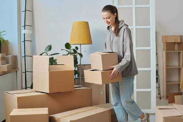 Young woman carrying packed boxes to the room during moving