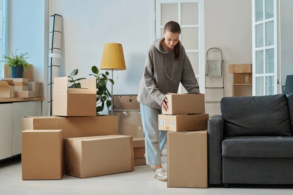 Young woman packing things in cardboard boxes in the room during moving to a new house