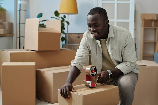 Joven Afroamericano Empacando Cosas Cajas Cartón Usando Cinta Adhesiva Durante —  Fotos de Stock