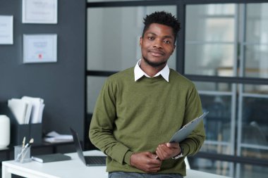 Afrikalı Amerikalı iş adamının portresi modern ofiste arka planda işyeriyle kameraya bakıyor.