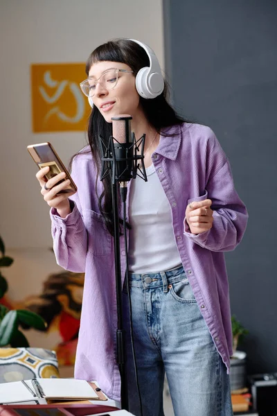 戴耳机的年轻女人用她的智能手机用麦克风唱歌 — 图库照片