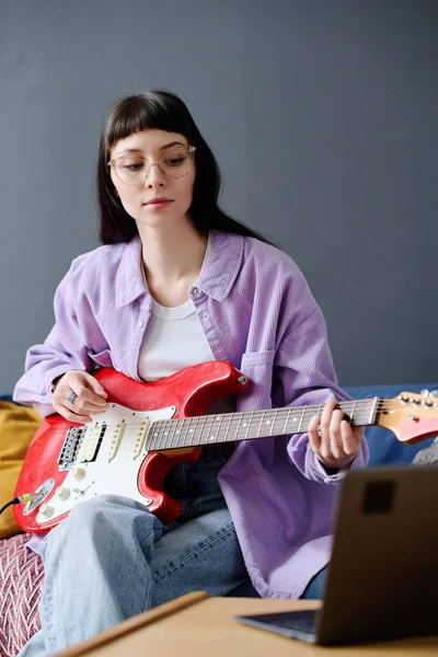 年轻女子专心致志地弹吉他 她看着手提电脑的监视器 学习弹奏吉他 — 图库照片