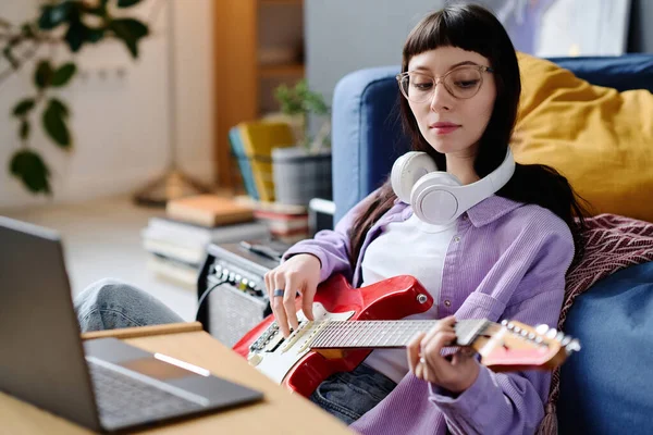 年轻女子坐在笔记本电脑前 弹吉他 她把自己的歌记录在电脑上 — 图库照片