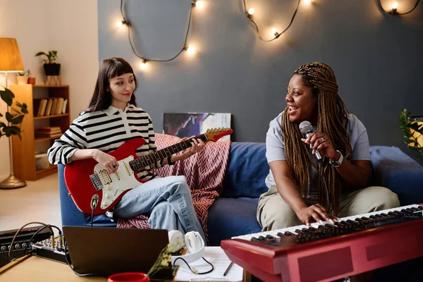 两个女孩坐在沙发上 用话筒和乐器在录音室里一起演奏音乐 — 图库照片