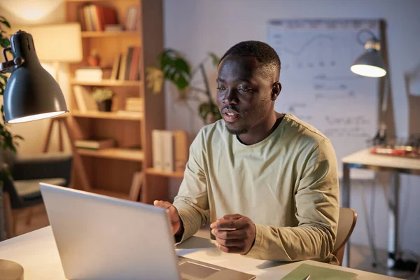 アフリカの若いビジネスマンは職場に座って同僚とノートパソコンでオンラインで話をしてオフィスでビジネスミーティングをしています — ストック写真