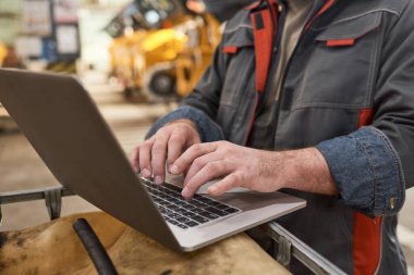 Dizüstü bilgisayarda yazan ve depoda dururken internetten çalışan üniformalı mühendislere yakın plan.