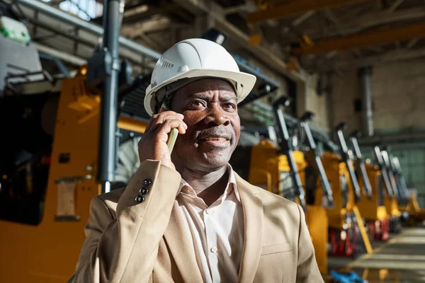공장에서의 절하면서 전화로 대화를 나누는 작업용 헬멧을 아프리카의 신뢰할 기술자 — 스톡 사진