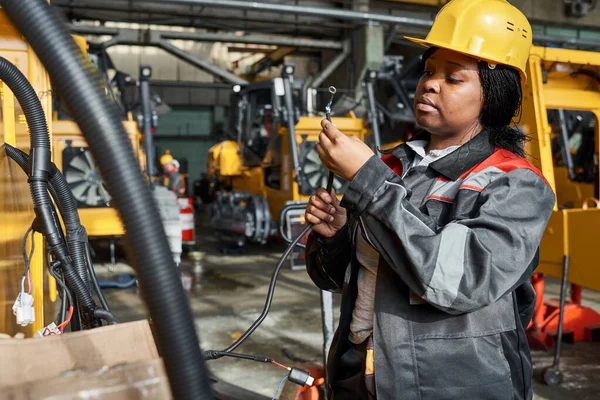 African female worker in uniform connecting wires to equipment during her work in warehouse