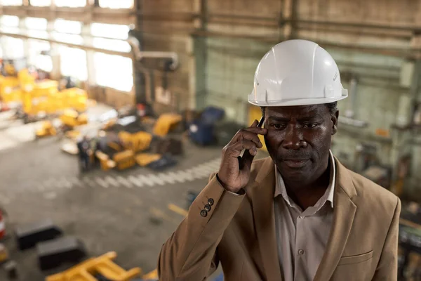 헬멧을 일하는 아프리카 엔지니어는 식물에 파트너와 전화로 얘기하는 입니다 — 스톡 사진