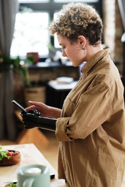Protez kollu bir kız mutfaktaki masada yemek fotoğrafı çekmek için cep telefonunu kullanıyor.