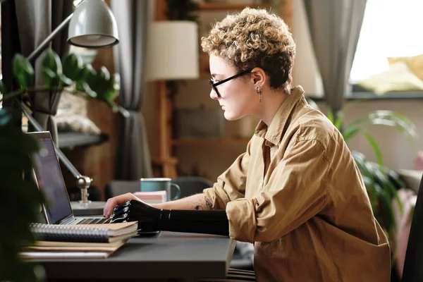 stock image Young woman with prosthetic arm typing on laptop at desk, she working online at home