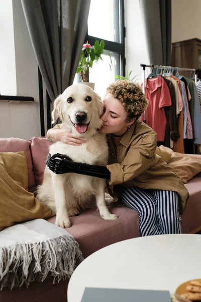 Woman with prosthetic arm embracing her cute golden retriever on the sofa in living room
