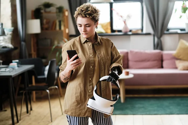 Girl with prosthetic arm using her smartphone to connect virtual reality goggles, she standing in living room