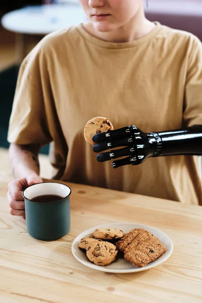 Close-up of girl with prosthetic arm drinking hot tea with homemade cookies at table