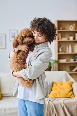 Dikey olarak, kollarında köpeği tutan ve odada dururken onu kucaklayan genç bir kadının görüntüsü.
