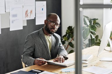 İş yerinde otururken gözlüklü Afrikalı işadamı kitap okuyor.