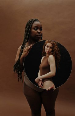 Afrikalı kilolu bir kadının portresi kahverengi arka planda duruyor ve elinde zayıf bir kadının portresi var.
