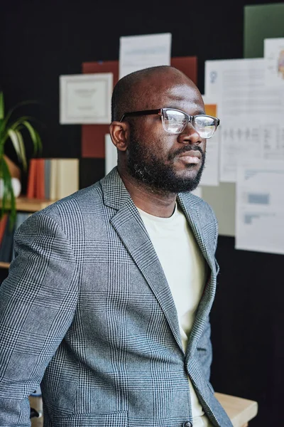 オフィスに立っている間に思慮深く見える眼鏡のアフリカの重大なビジネスマン — ストック写真
