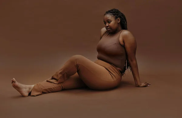 Zwart Mollige Vrouw Zoek Pensive Zittend Tegen Bruine Achtergrond — Stockfoto