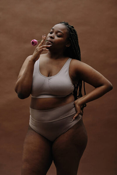 Портрет африканской молодой женщины с пухлой формой, курящей розовый цветок в качестве сигареты