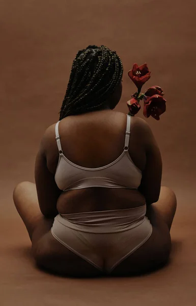 Achteraanzicht Van Afrikaanse Vrouw Met Overgewicht Zittend Ondergoed Bloem Vasthoudend — Stockfoto