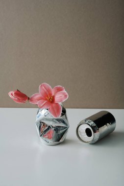 Dikey, taze pembe çiçekler ve iki alüminyum içecek kutusu, açık gri kahverengi duvar arka planı, geri dönüşüm konsepti.