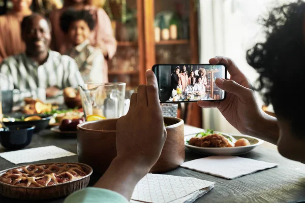 Evdeki tatil yemeği sırasında cep telefonuyla büyük ailesinin fotoğrafını çeken genç adam.