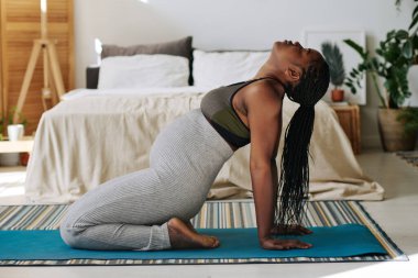 Afrikalı genç bir kadın, hamileliği boyunca yatak odasındaki egzersiz paspasına gözlerini kapatarak meditasyon yapıyor.