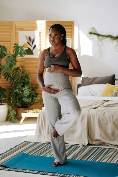 非洲年轻女子在做瑜伽的时候摸着怀孕的肚子 在卧室的练习垫上摆着姿势 — 图库照片