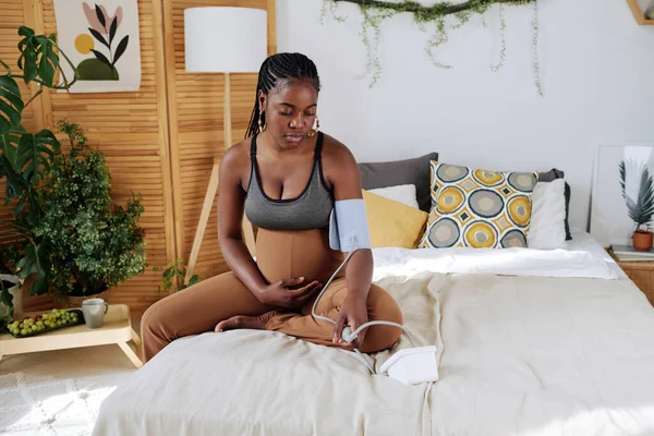 年轻的孕妇坐在床上摸着肚子 测量血压 — 图库照片