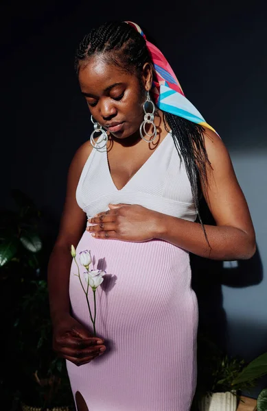 非洲孕妇抱着美丽的花朵在怀孕的肚子前等待着孩子的出生 — 图库照片