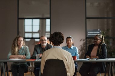 İş görüşmeleri sırasında kendisine sorular soran iş adamlarının karşısındaki sandalyede oturan genç adamın arka görünüşü.