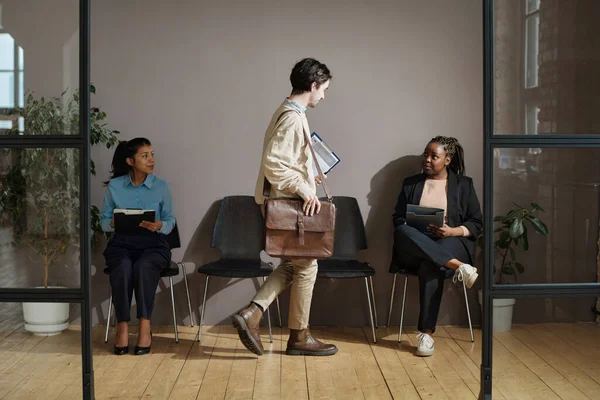 stock image Young man with suitcase sitting on chair between two women in office corrifor