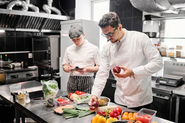 Joven Chef Uniforme Eligiendo Verduras Frescas Para Plato Mesa Con — Foto de Stock