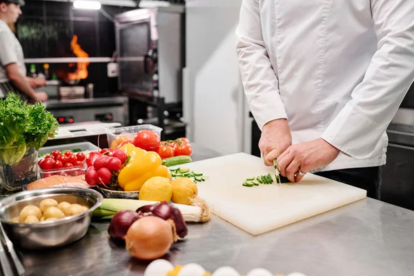 stock image Close-up of cook in uniform cutting fresh vegetable on cutting board at table during work in kitchen