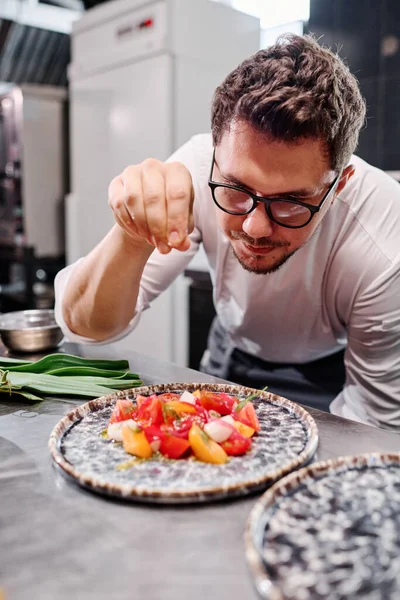 Joven Chef Anteojos Añadiendo Especias Ensalada Verduras Plato Mientras Cocina — Foto de Stock