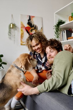 Gülümseyen, etnik çeşitliliğe sahip bir çift evdeki kanepede dinleniyor ve köpekleriyle oynuyor.