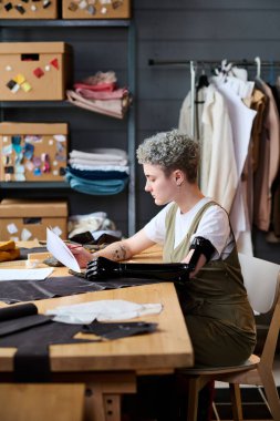 Myoelektrik kollu genç ciddi moda tasarımcısının çizimlere bakarken yeni kolej kıyafetleri üzerinde çalışmasının yan görüntüsü