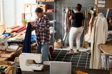 Geniş atölyede yaratıcı moda koleksiyonu üzerinde çalışırken yeni kıyafetler için tekstil seçen iki kültürlü genç.