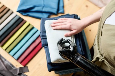 Yeni sezonluk moda koleksiyonu için hazırlanmış katlanmış tekstil yığınının üzerinde miyoelektrik koluyla genç kadın terzinin elleri.