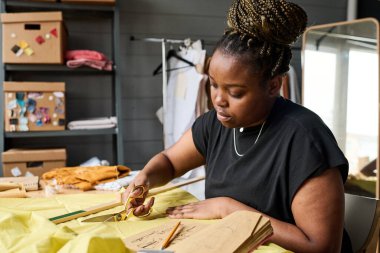 Moda koleksiyonu için yeni moda ürünler yaratmaya çalışırken makaslı genç ciddi terzi sarı renkli tekstil kesiyor.