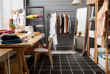 Geniş aynalı, raflı, katlanmış tekstil ve dikiş makineli modern moda tasarımcısının geniş atölyesi.